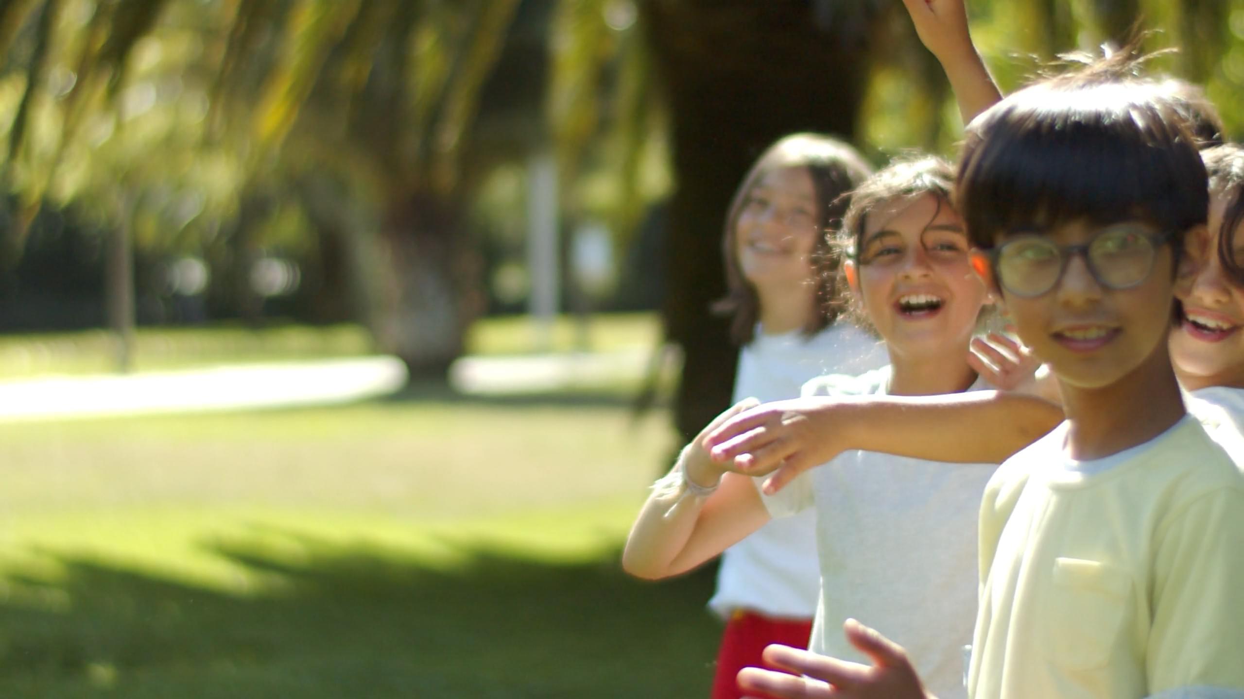 A girl in motion high-fives a row of children with outstretched hands, smiling as she runs across the grassy field on a sunny day