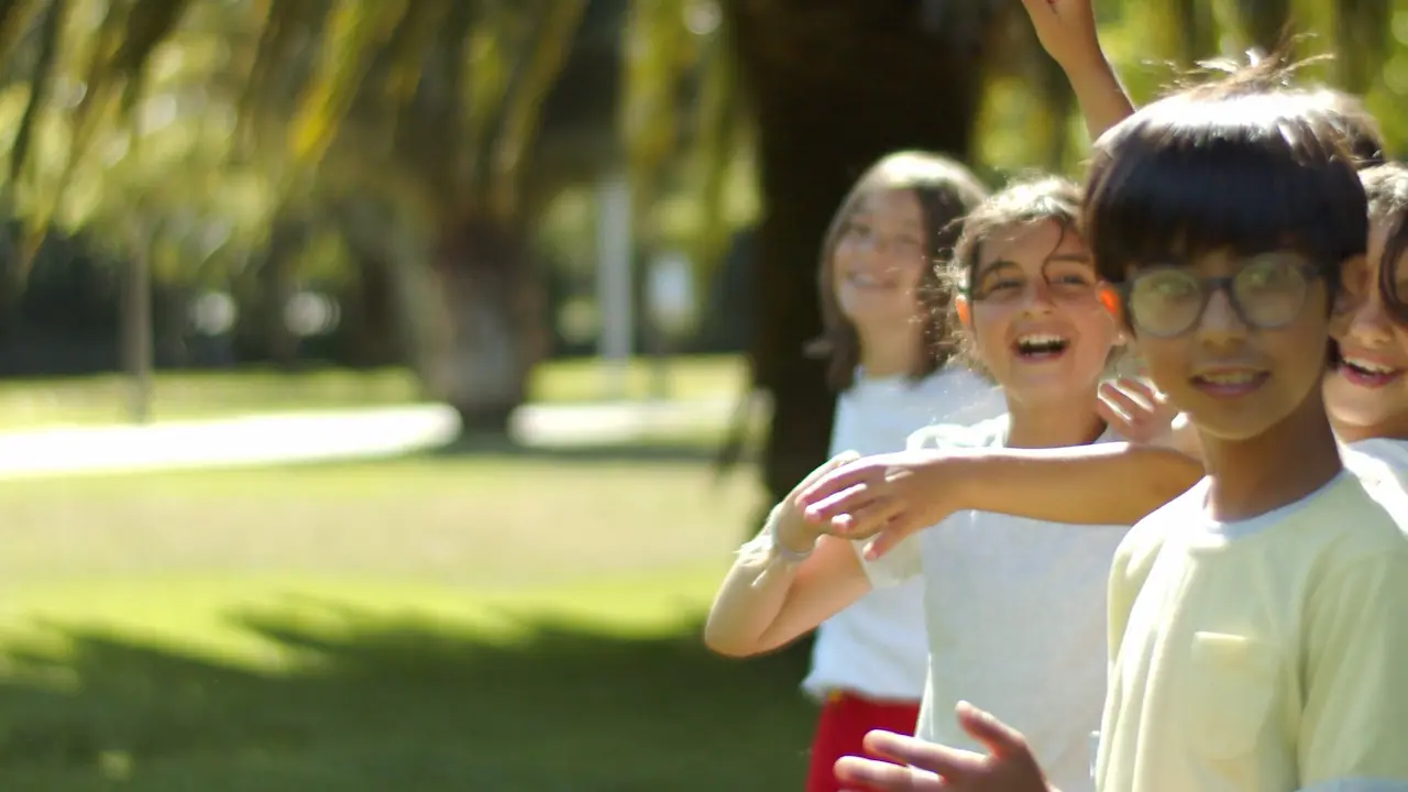 A group of children stand on the right side of the frame, smiling warmly toward the viewer against a backdrop of green grass.